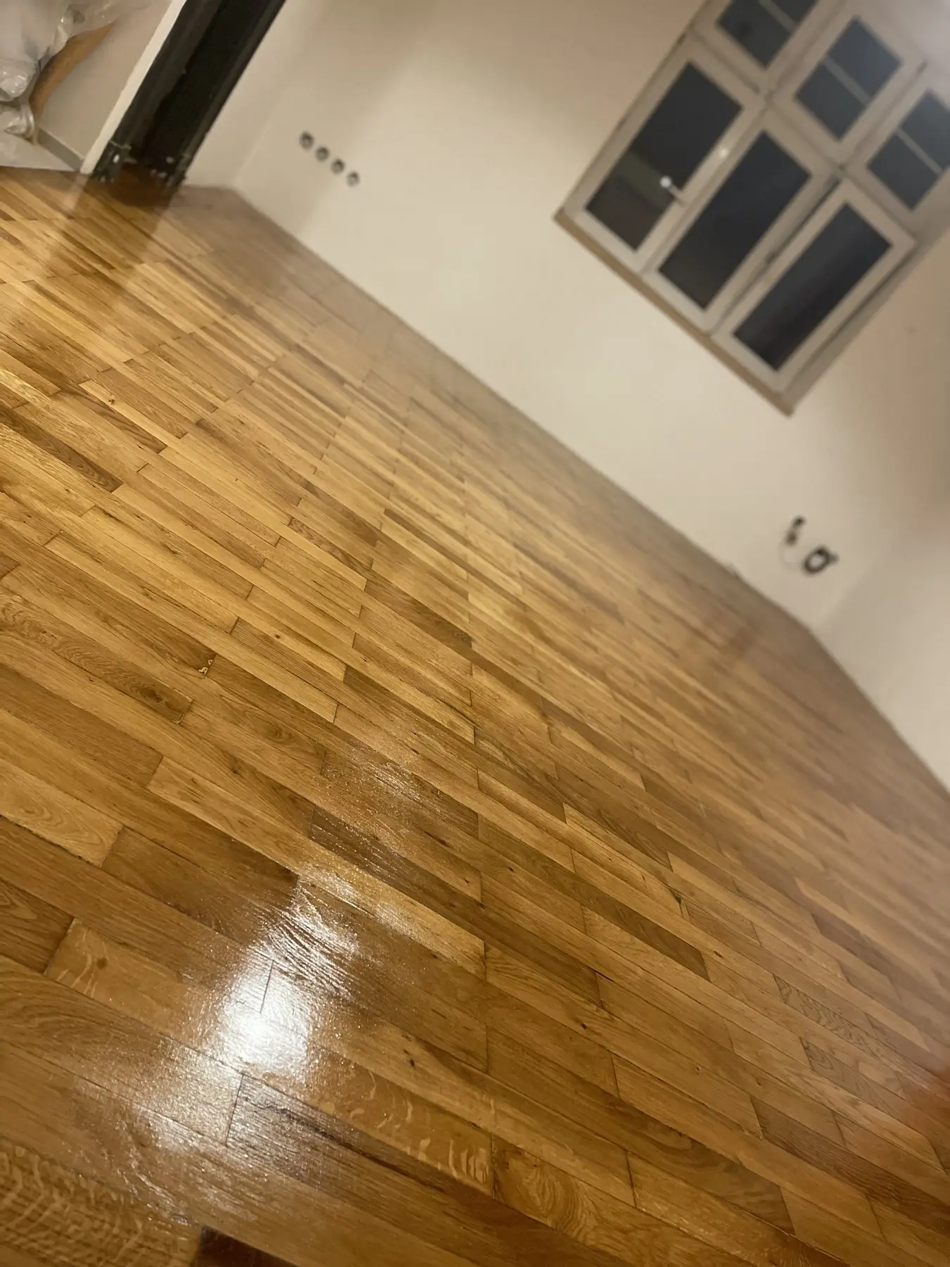 Dubové parkety po renovaci, nově nalakované, v prázdném světlém pokoji s oknem